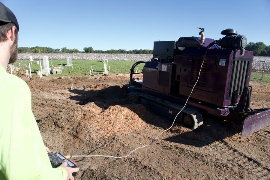 Remote-controlled tracked stump grinder working beside a pile of fresh wood chips