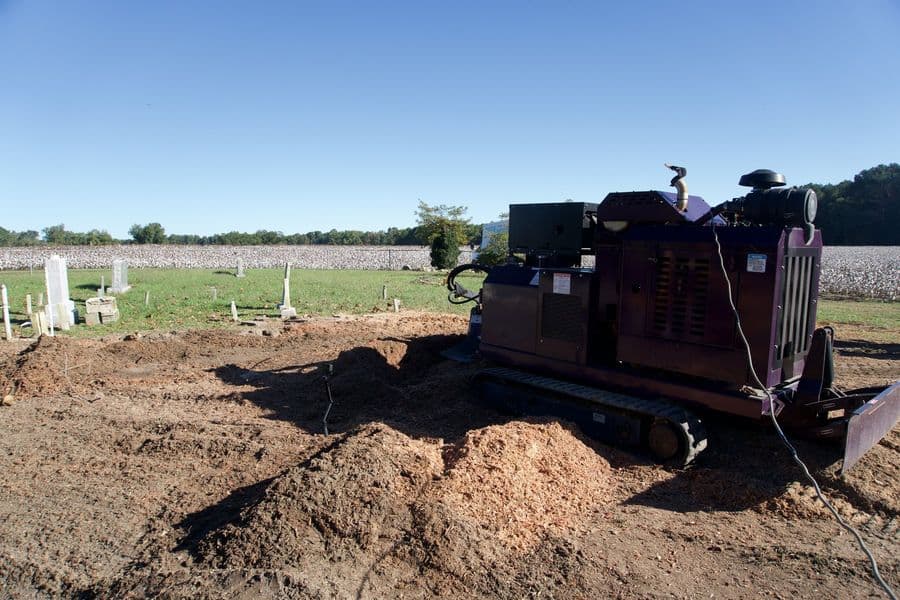 Tracked stump grinder beside a small cemetery at the edge of a cotton field