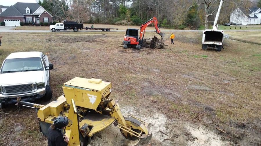 Stump grinder, excavator and bucket truck working together on a cleared neighborhood lot